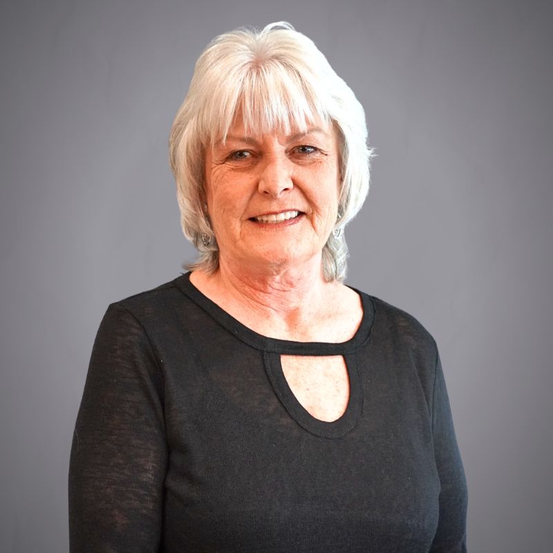 Access Headshots - Access Title & Escrow Older woman with short white hair wearing a black top, smiling, against a gray studio backdrop (portrait).